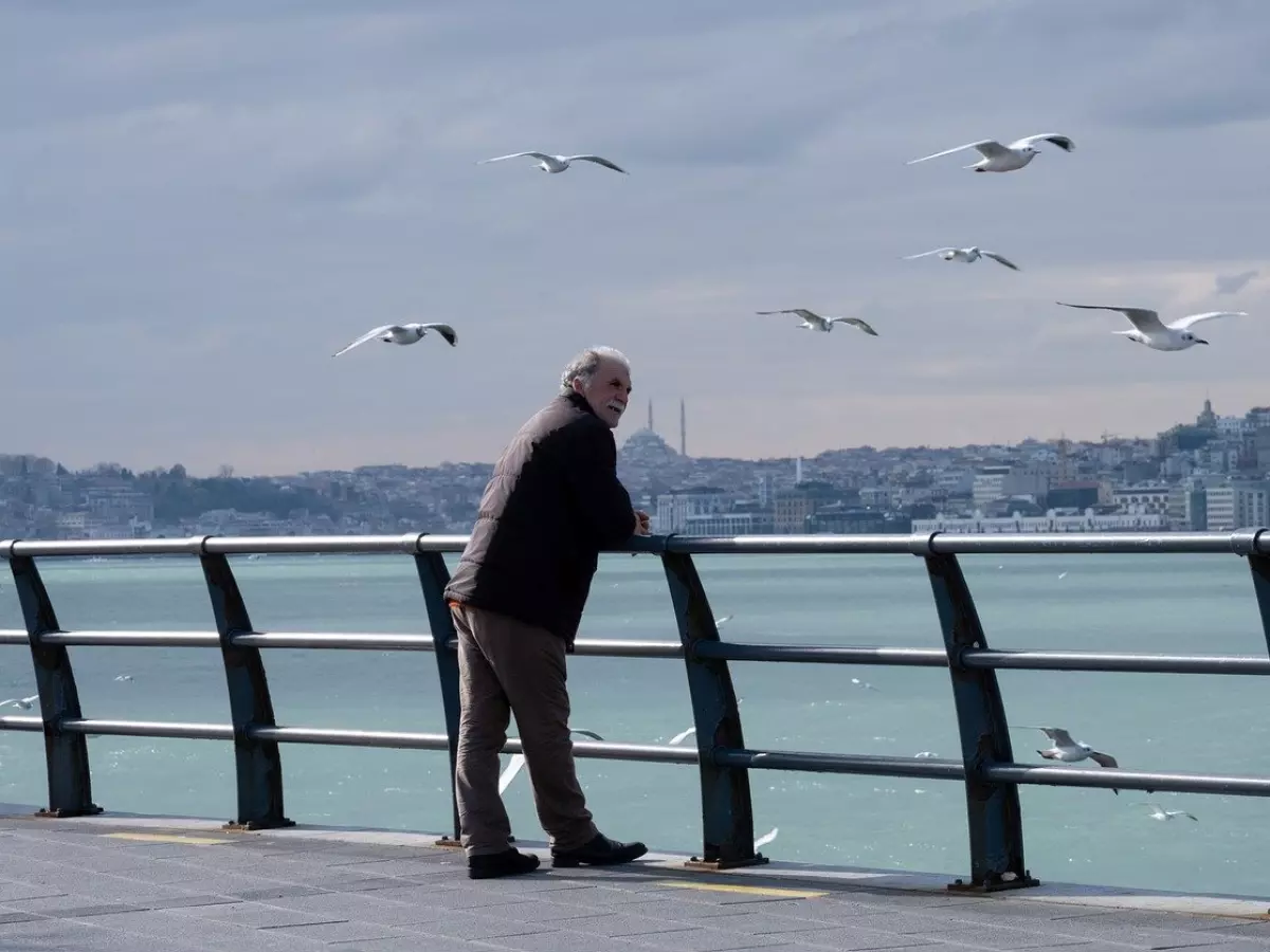 An older man with grey hair is standing on a pier overlooking the sea.