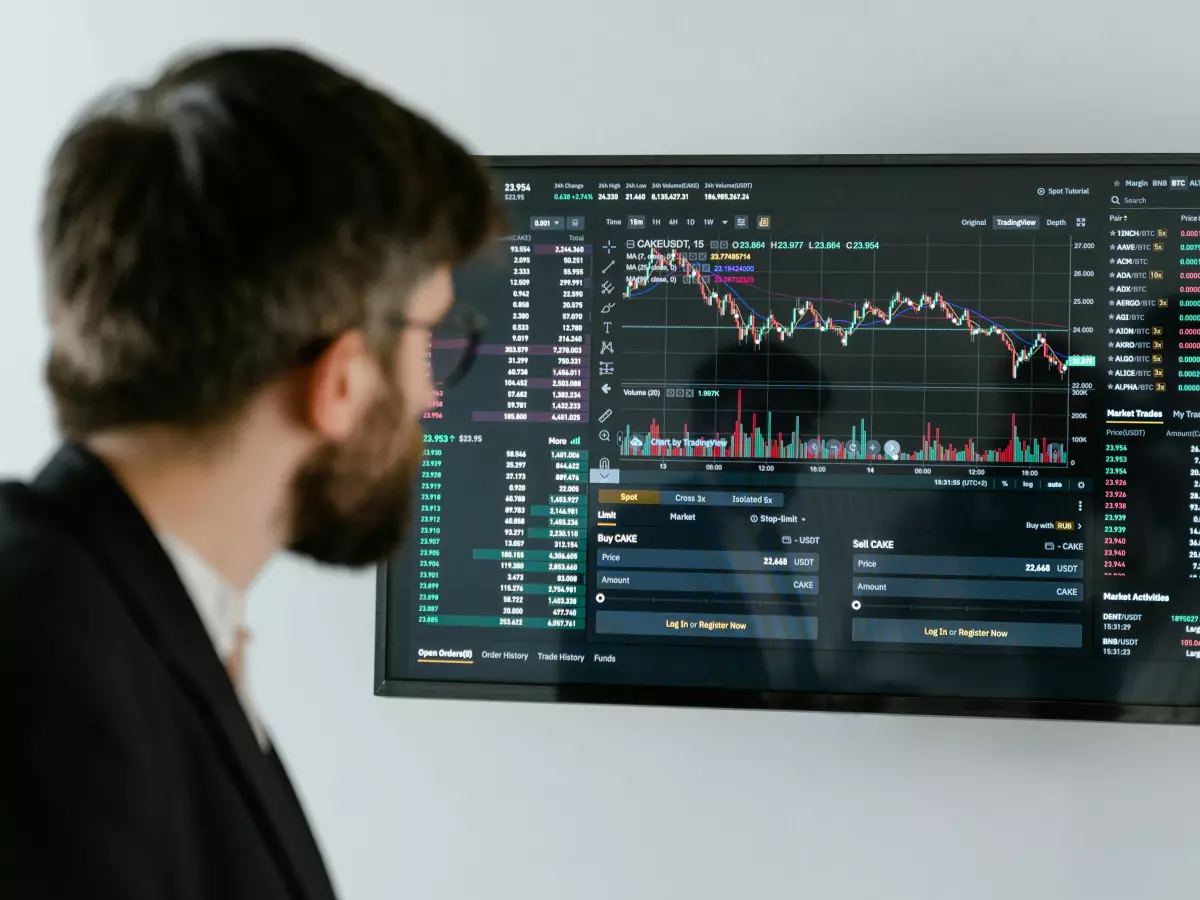 A man in a suit stands in front of a large screen displaying financial data. He appears to be analyzing the data, with a focused expression on his face.