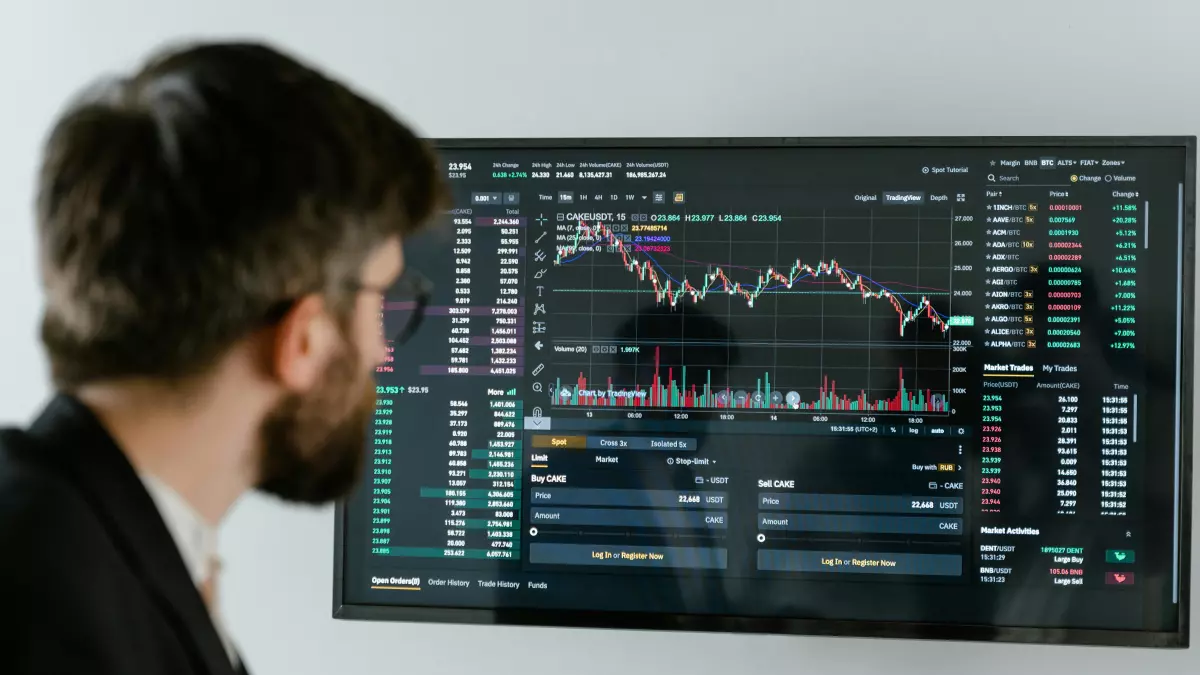 A man in a suit stands in front of a large screen displaying financial data. He appears to be analyzing the data, with a focused expression on his face.