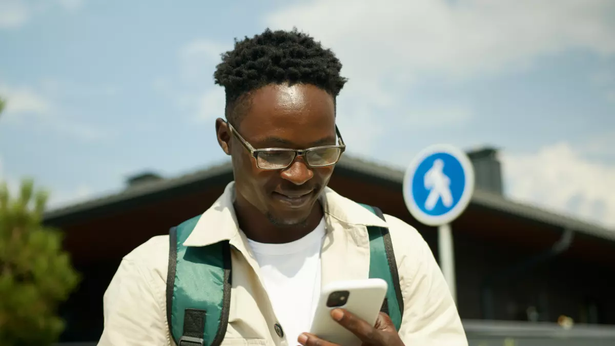 A man is smiling while looking at his phone outdoors.