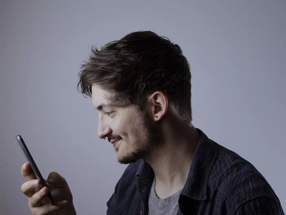 A young man is looking at his smartphone, he is smiling