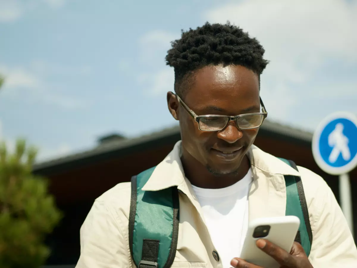 A man is smiling while looking at his phone outdoors.