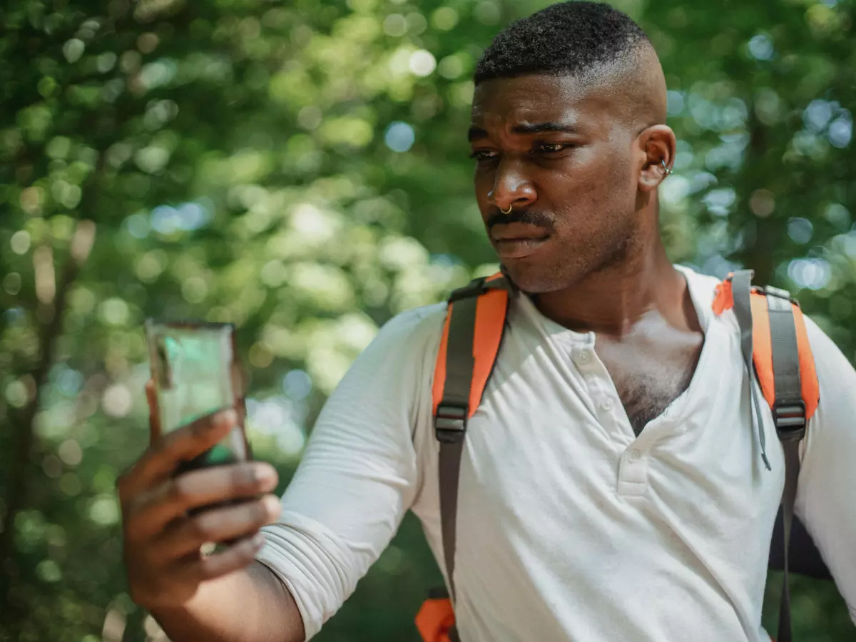 A man with a backpack looks at his phone in a forest.