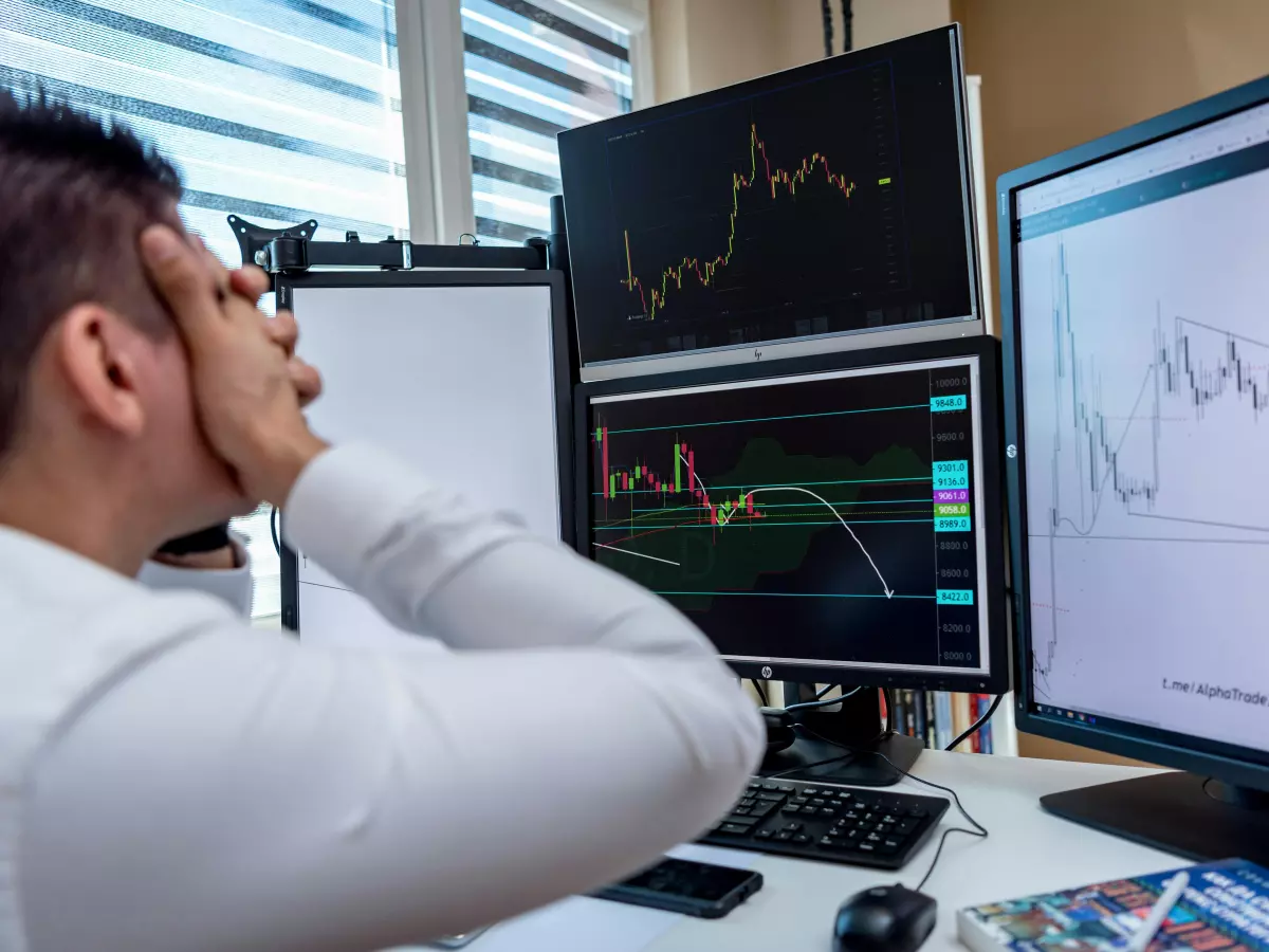 A person looking intently at multiple computer screens displaying stock market graphs, highlighting the volatility and complexity of tech stock investments.