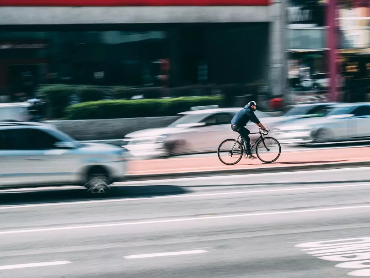 A cyclist is riding on the road. A car is passing by on the left side.