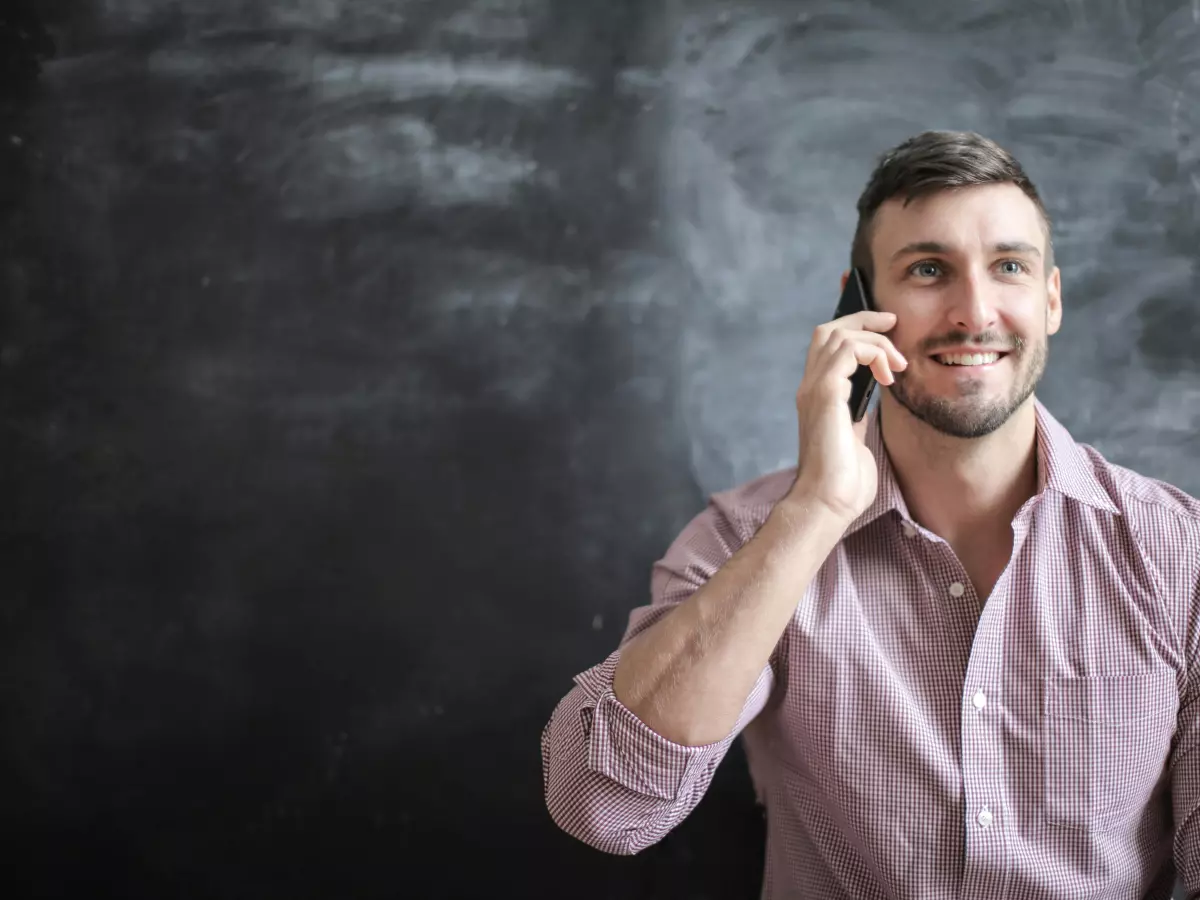 A man is smiling and talking on a smartphone against a dark background.