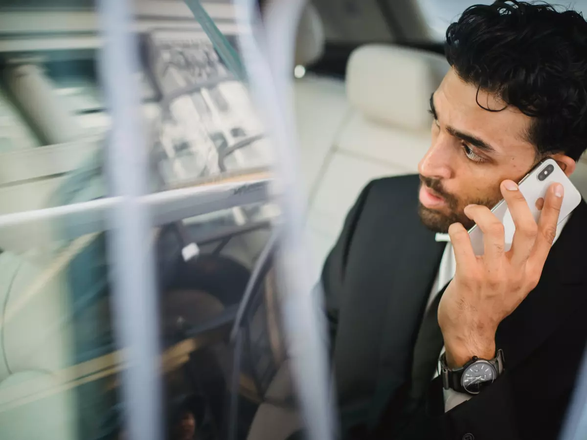 A man in a suit, sitting in the back seat of a car, is talking on his phone.