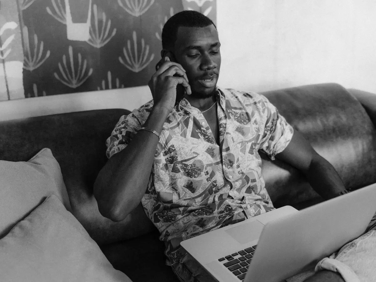 A person sitting on a couch, using a Samsung phone and a laptop.