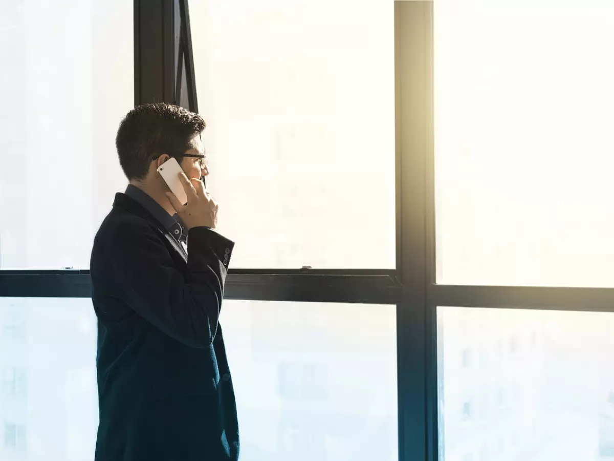 A young man in a suit looking out the window while talking on the phone