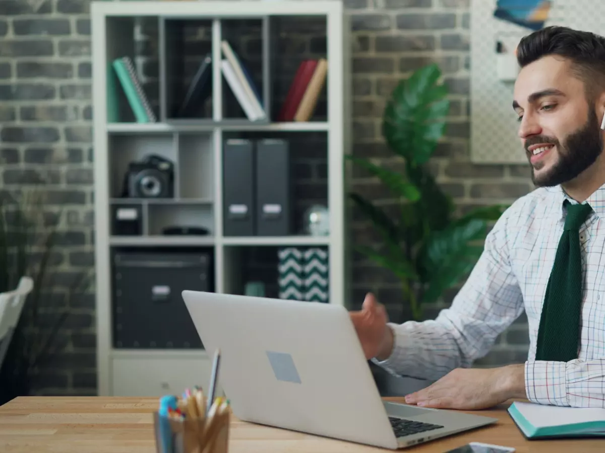 A man in a business suit is on a video call with someone on his laptop. He's smiling and gesturing with his hands.