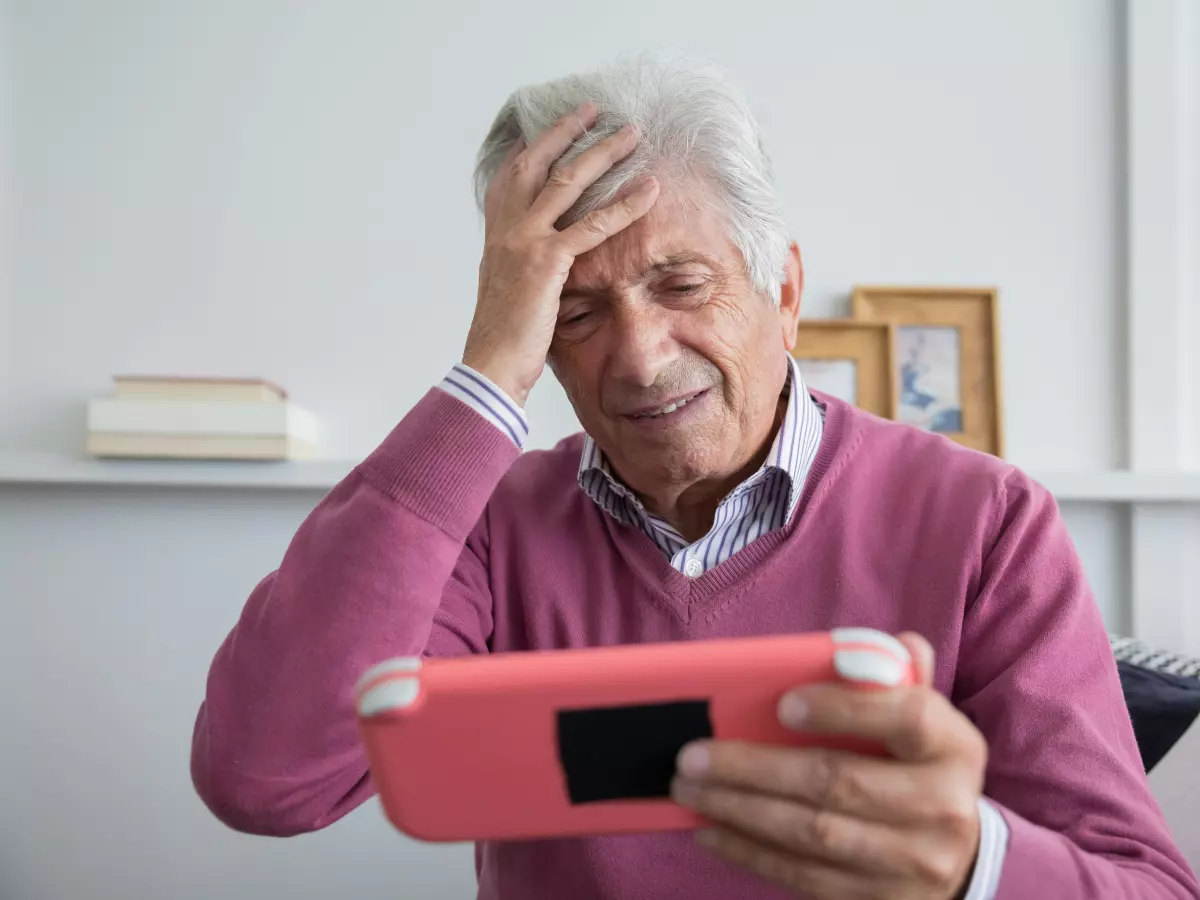 An elderly man in a pink sweater, playing a Nintendo DS game, looking frustrated. The image conveys a sense of nostalgia and a feeling of excitement for a new online feature.