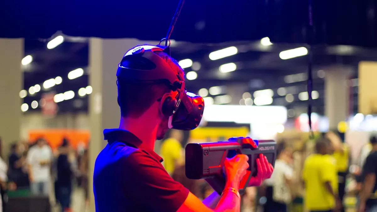 A person wearing VR headset holds a controller and is surrounded by people in a brightly lit environment.