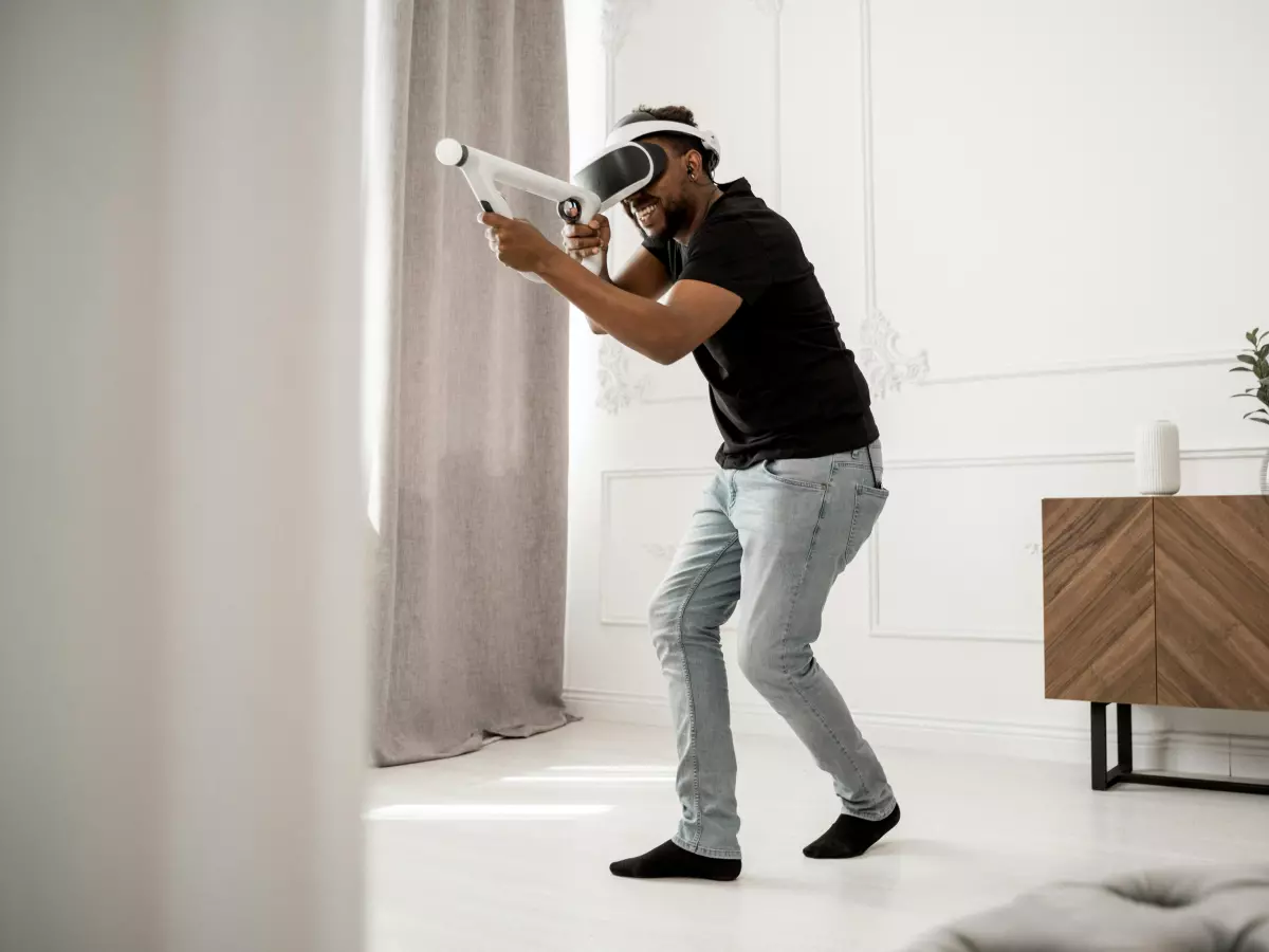 A man wearing a VR headset and holding a VR controller, standing in his living room, playing a VR game.