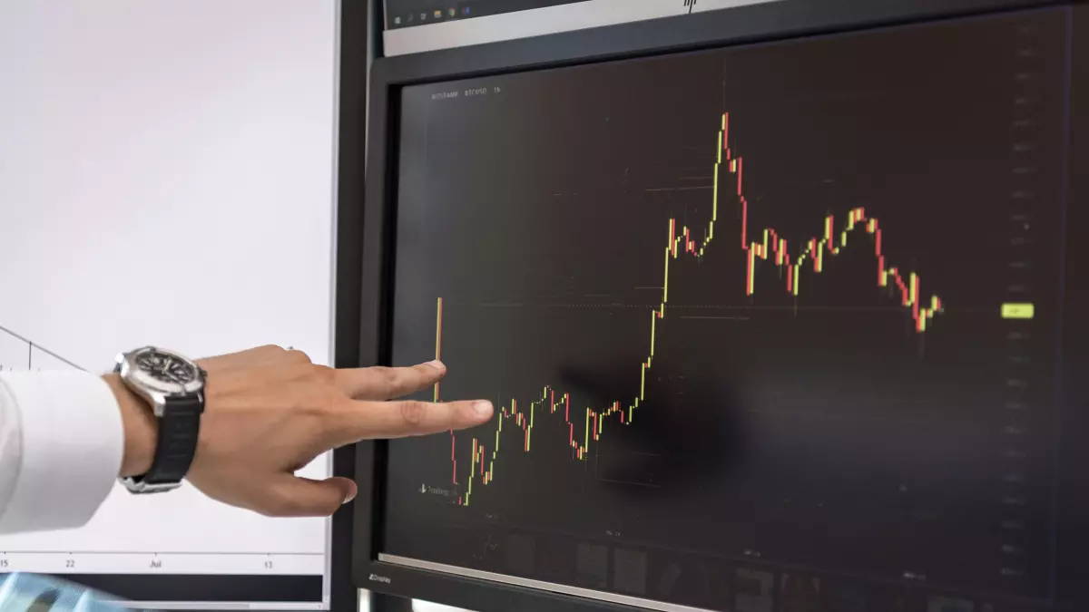 A hand pointing at a computer screen showing a stock market graph of cryptocurrency. 