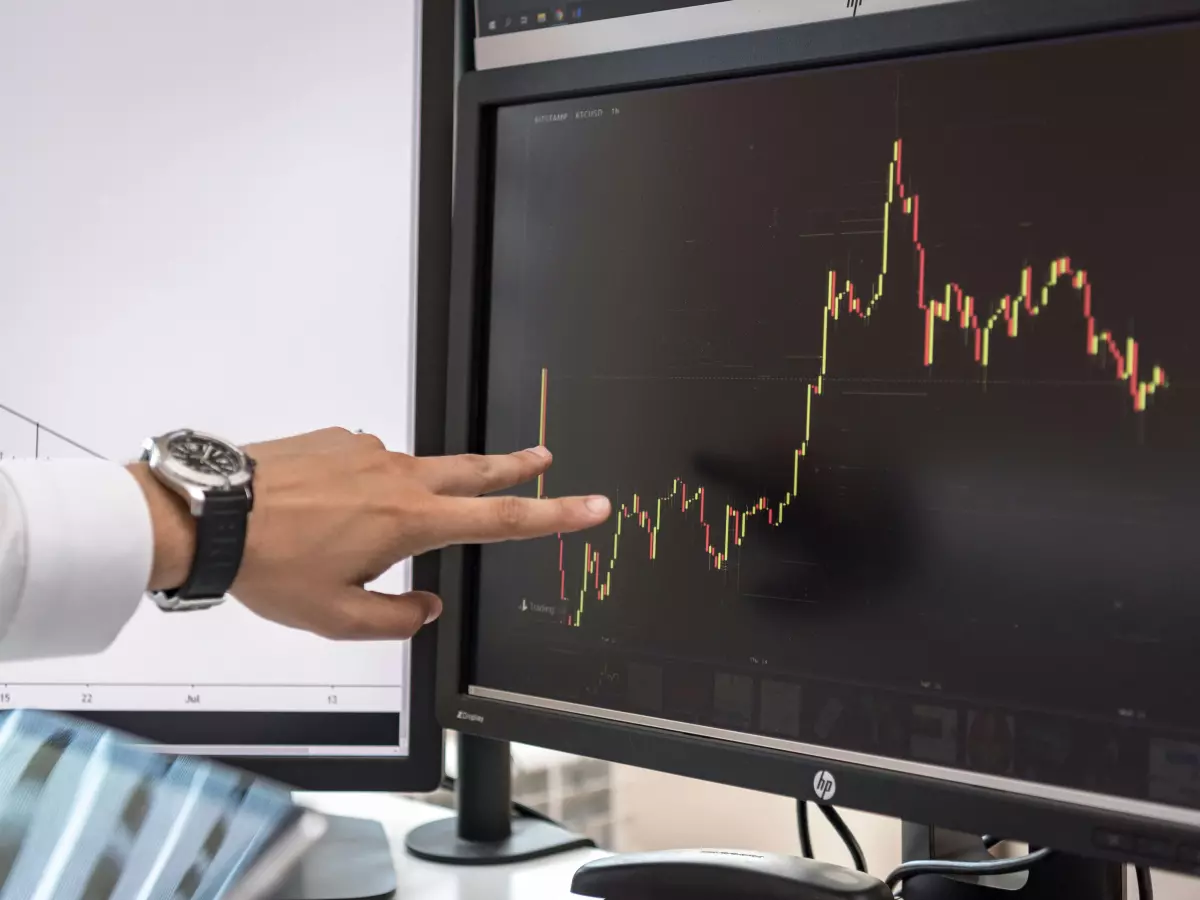 A hand pointing at a computer screen showing a stock market graph of cryptocurrency. 