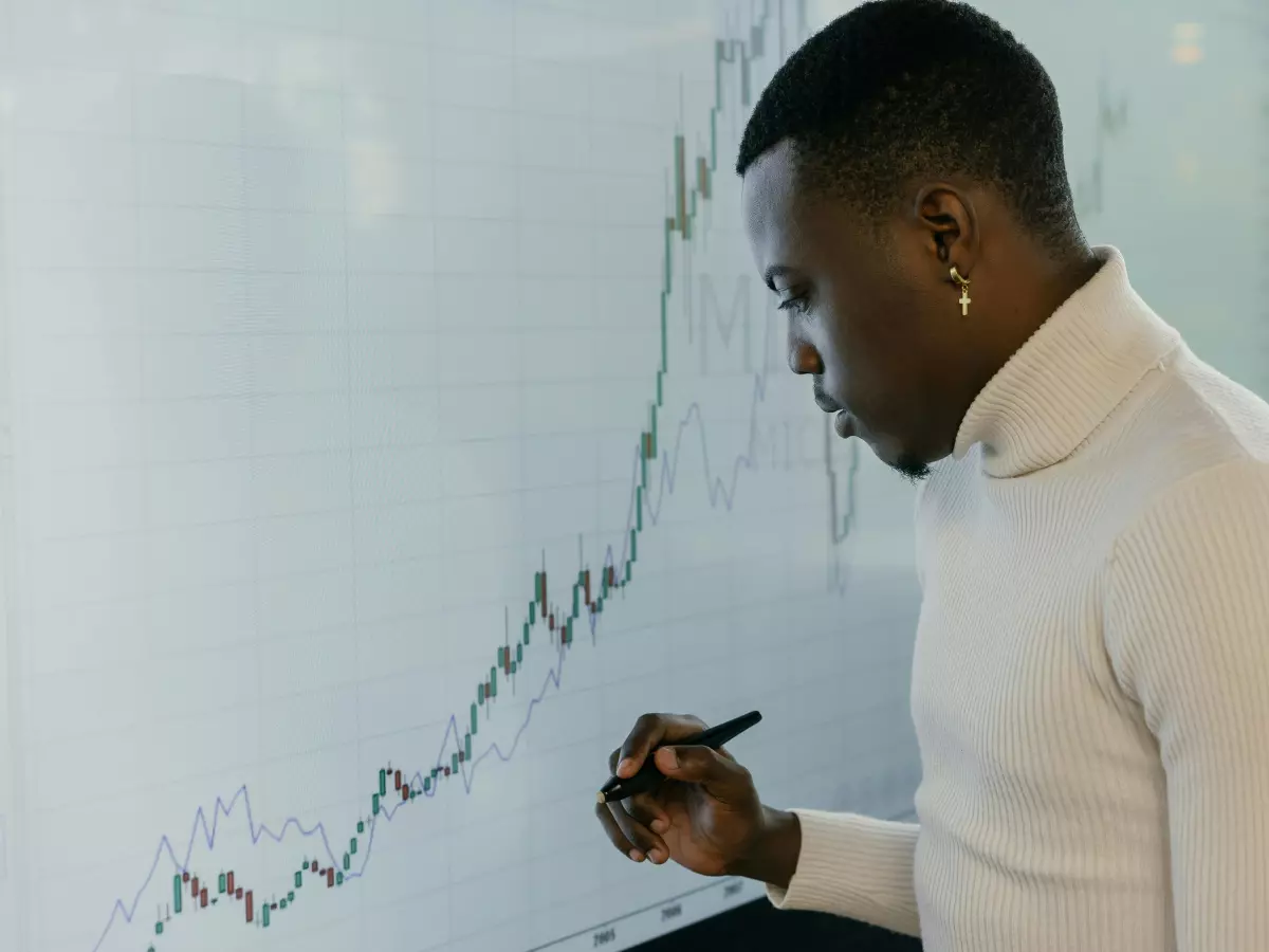 A man in a white turtleneck is drawing a graph on a whiteboard. He has his head down and is focused on the task at hand.