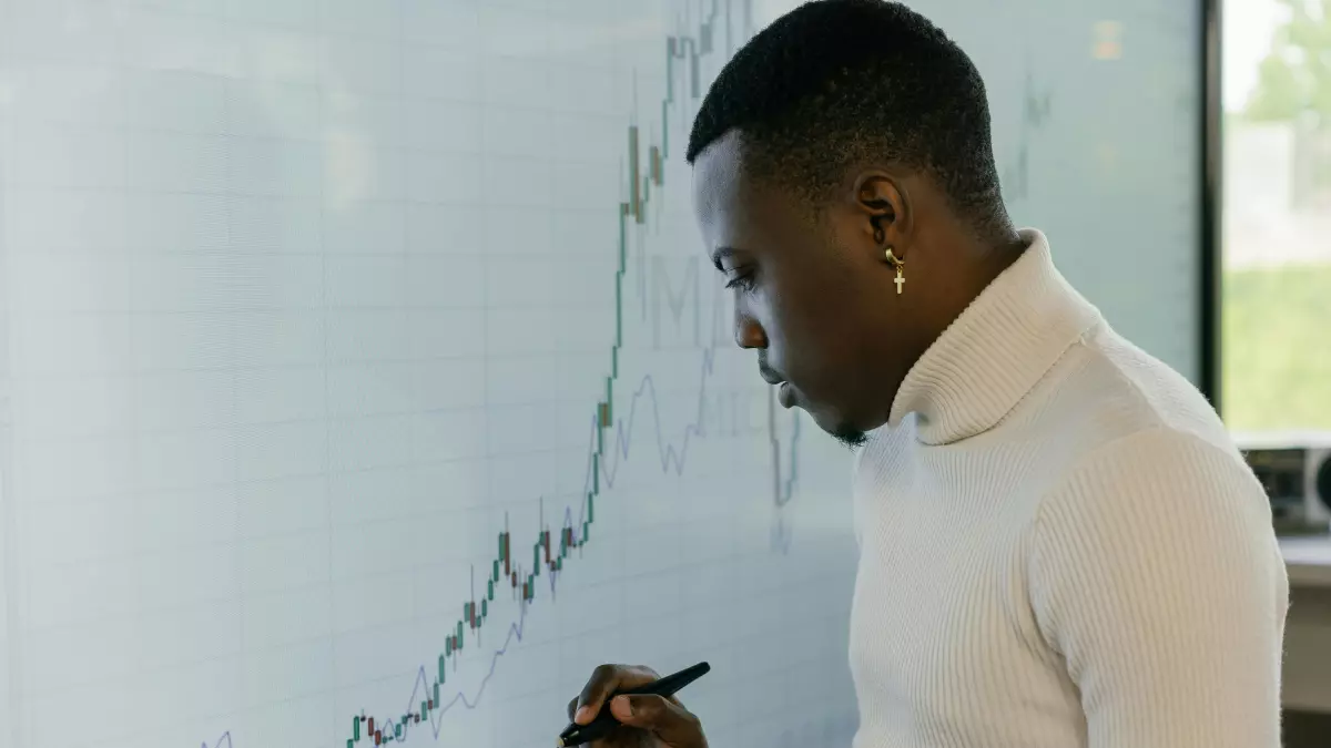 A man in a white turtleneck is drawing a graph on a whiteboard. He has his head down and is focused on the task at hand.