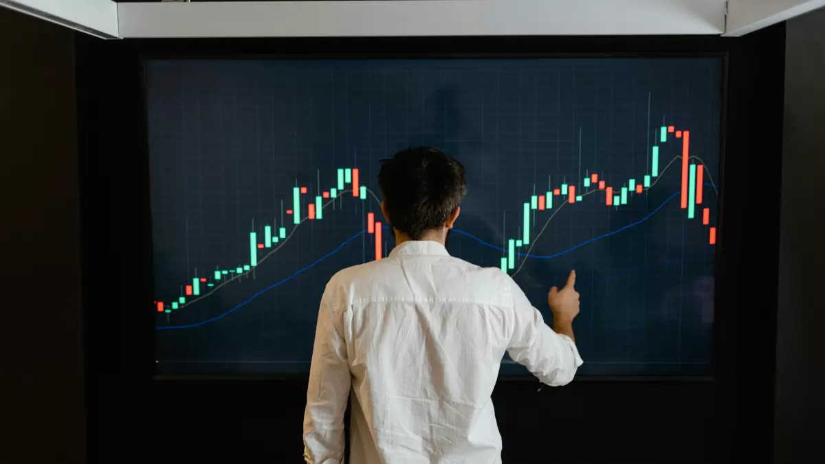 A person in a white shirt pointing at a large screen displaying a rising stock chart, symbolizing Bitcoin