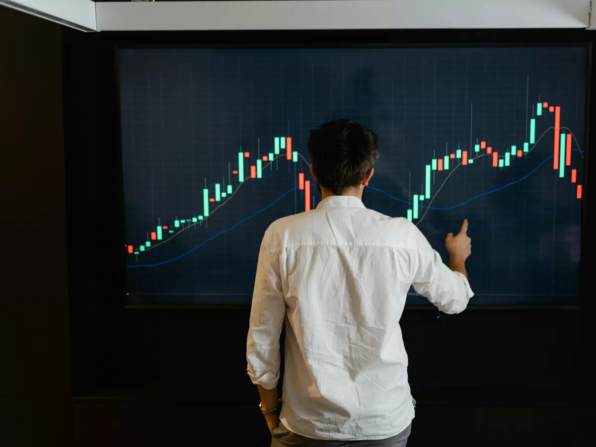 A person in a white shirt pointing at a large screen displaying a rising stock chart, symbolizing Bitcoin's surge.