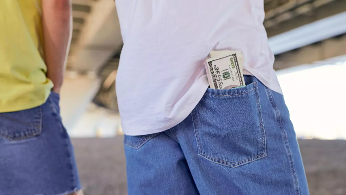 A man with a wad of cash in his back pocket, with his hands in his pockets.