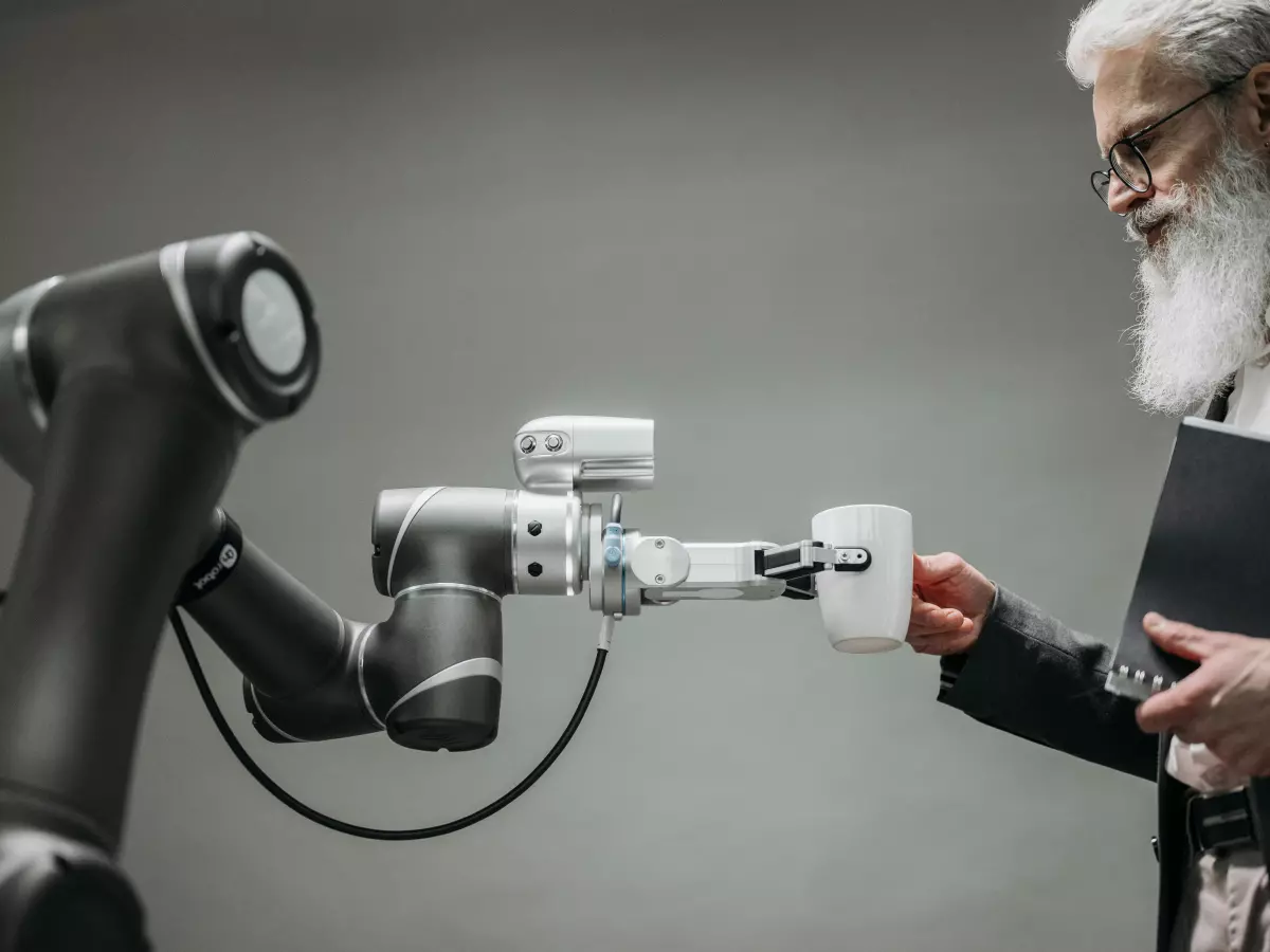 A robotic arm with multiple joints interacts with a human, holding a piece of paper, showcasing the integration of robotics and human interaction.