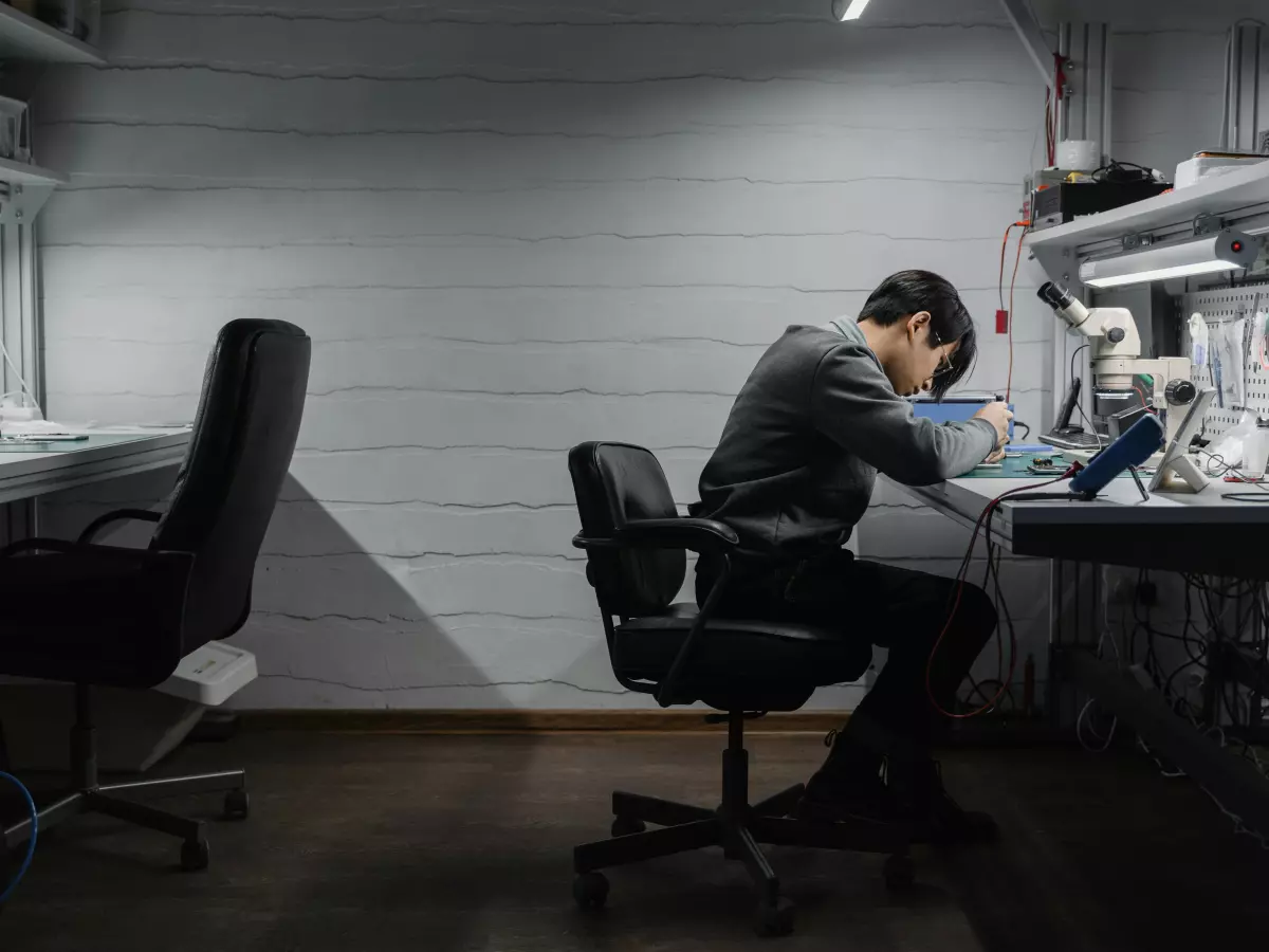 A man sits at a desk in a dimly lit room and looks intently at his computer.