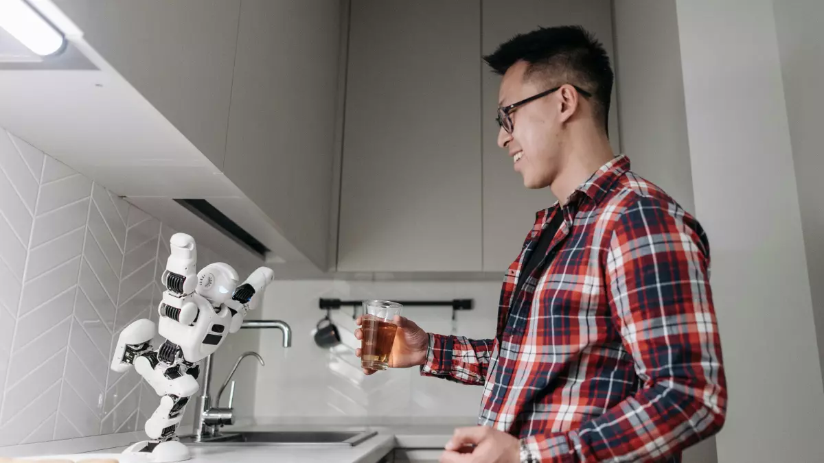 A man in a plaid shirt stands in a kitchen watching a robotic arm pour a cup of coffee.