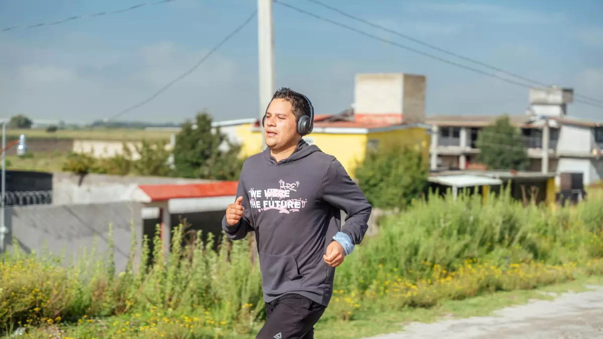 A young person wearing a grey hoodie and black shorts runs along a rural road with a blue sky in the background.