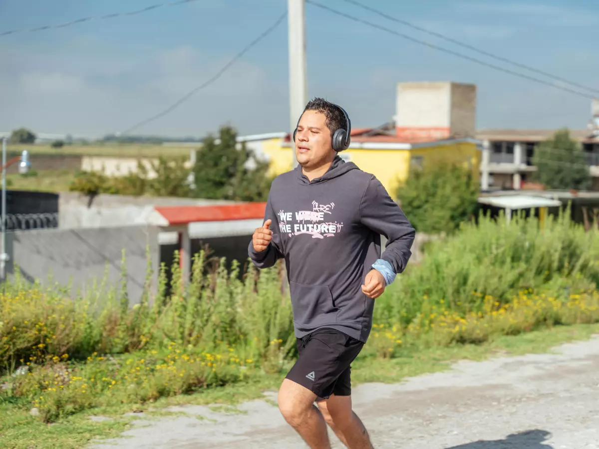 A young person wearing a grey hoodie and black shorts runs along a rural road with a blue sky in the background.