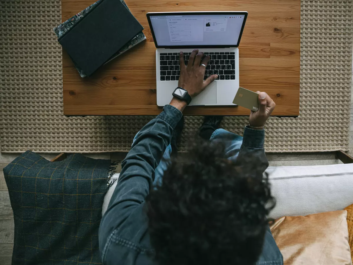 A person using a laptop computer to shop online, sitting on a couch with a credit card in hand.