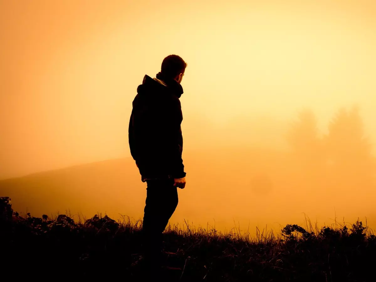 A man in a hooded jacket stands silhouetted against a foggy background, looking into the distance.