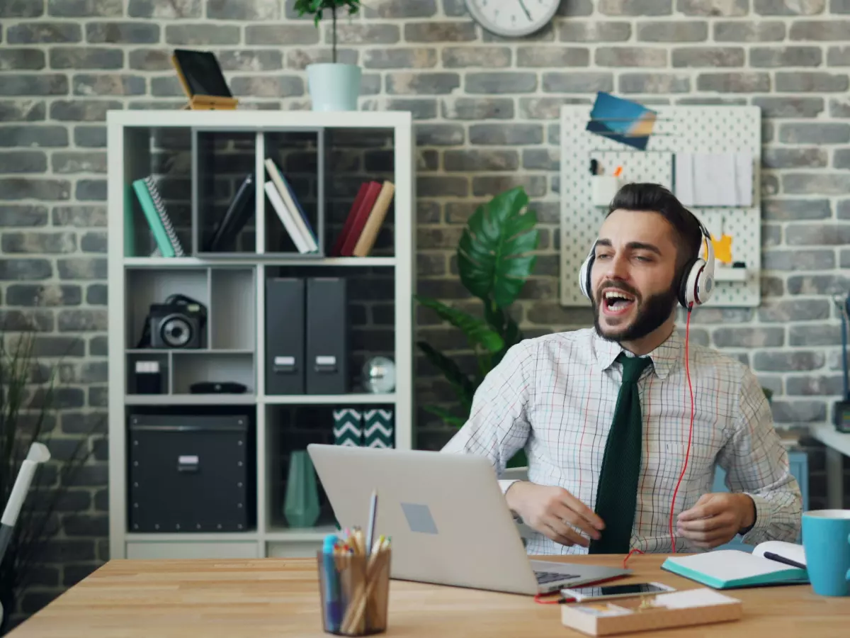 A man in a shirt and tie dances in his office while listening to music with headphones on. He appears to be enjoying himself.