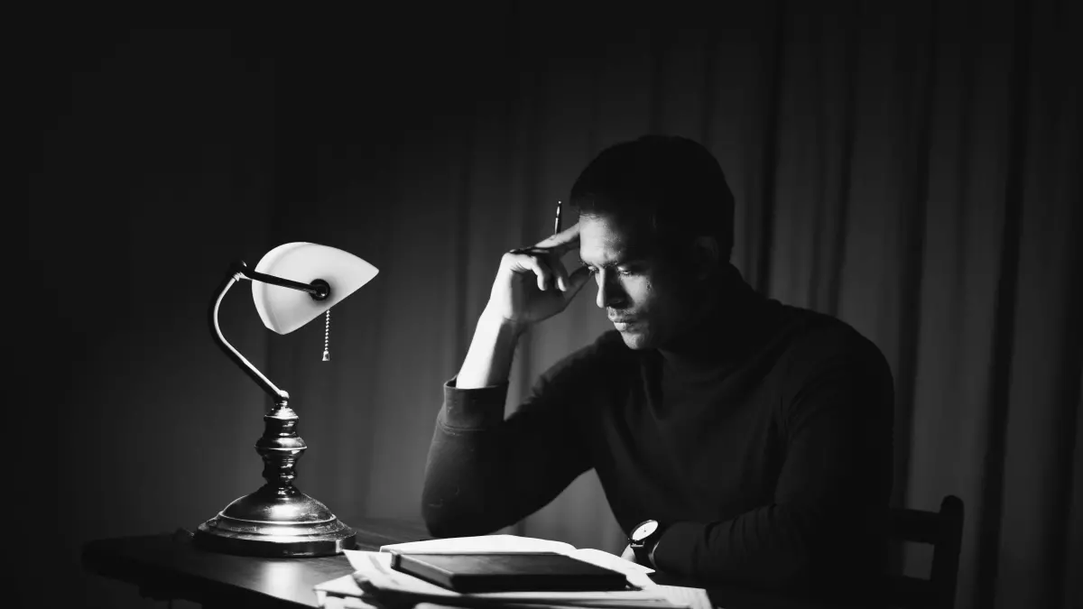 A person is reading a book in a dimly lit room. A table lamp illuminates the book and the person