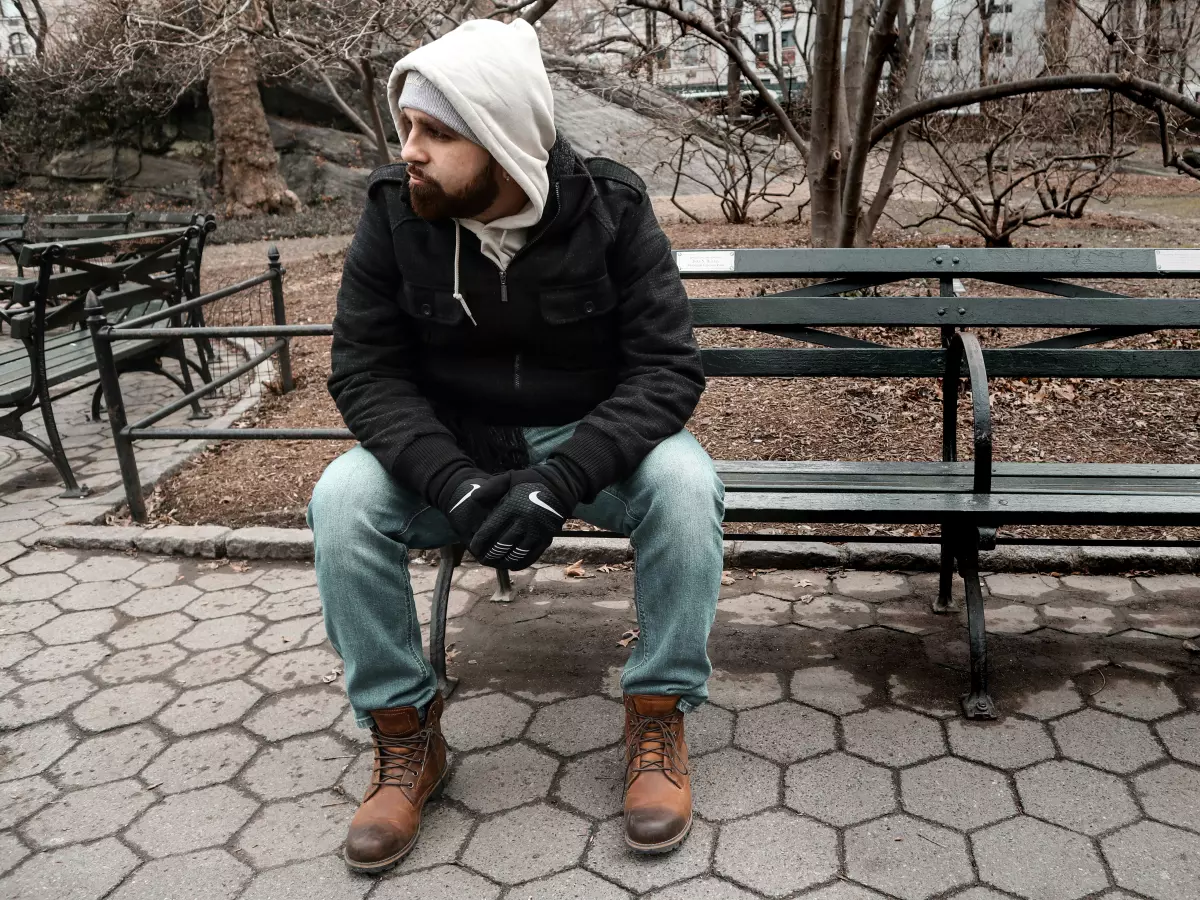 A man sitting on a bench in a park, looking down at his phone.