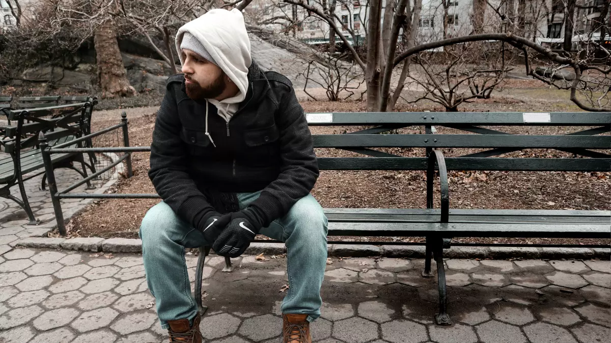 A man sitting on a bench in a park, looking down at his phone.