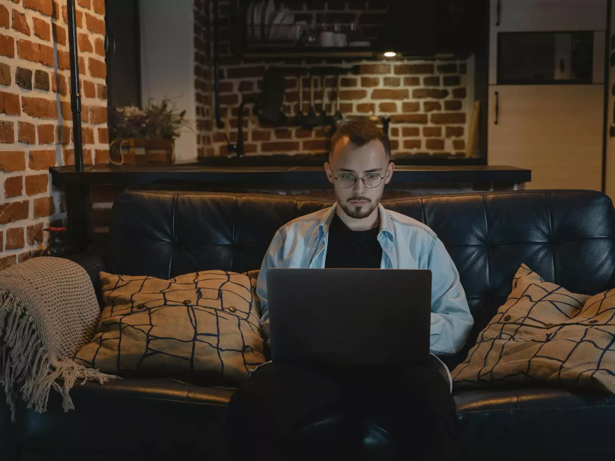 A man sitting on a sofa, working on a laptop in a living room.