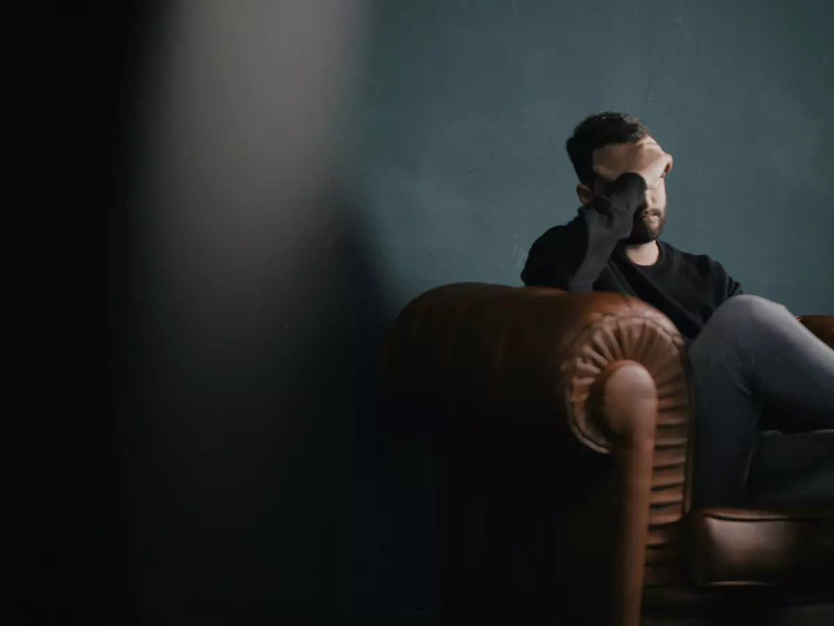 A man sitting in a leather armchair with his head in his hands looking overwhelmed.