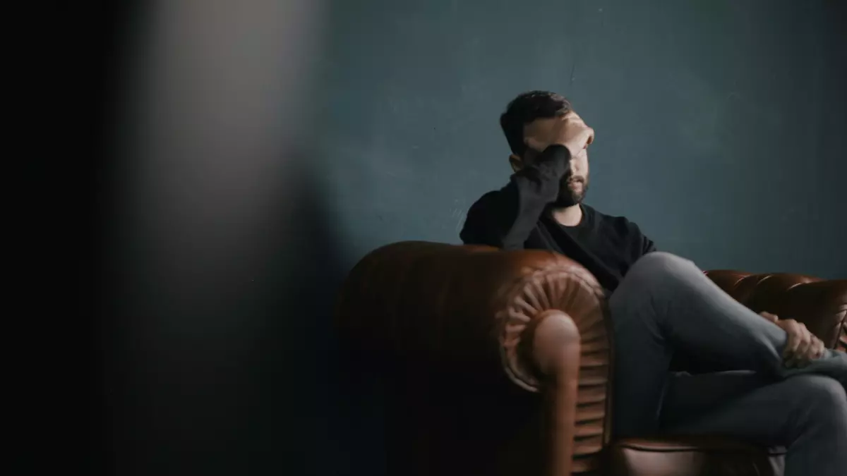 A man sitting in a leather armchair with his head in his hands looking overwhelmed.