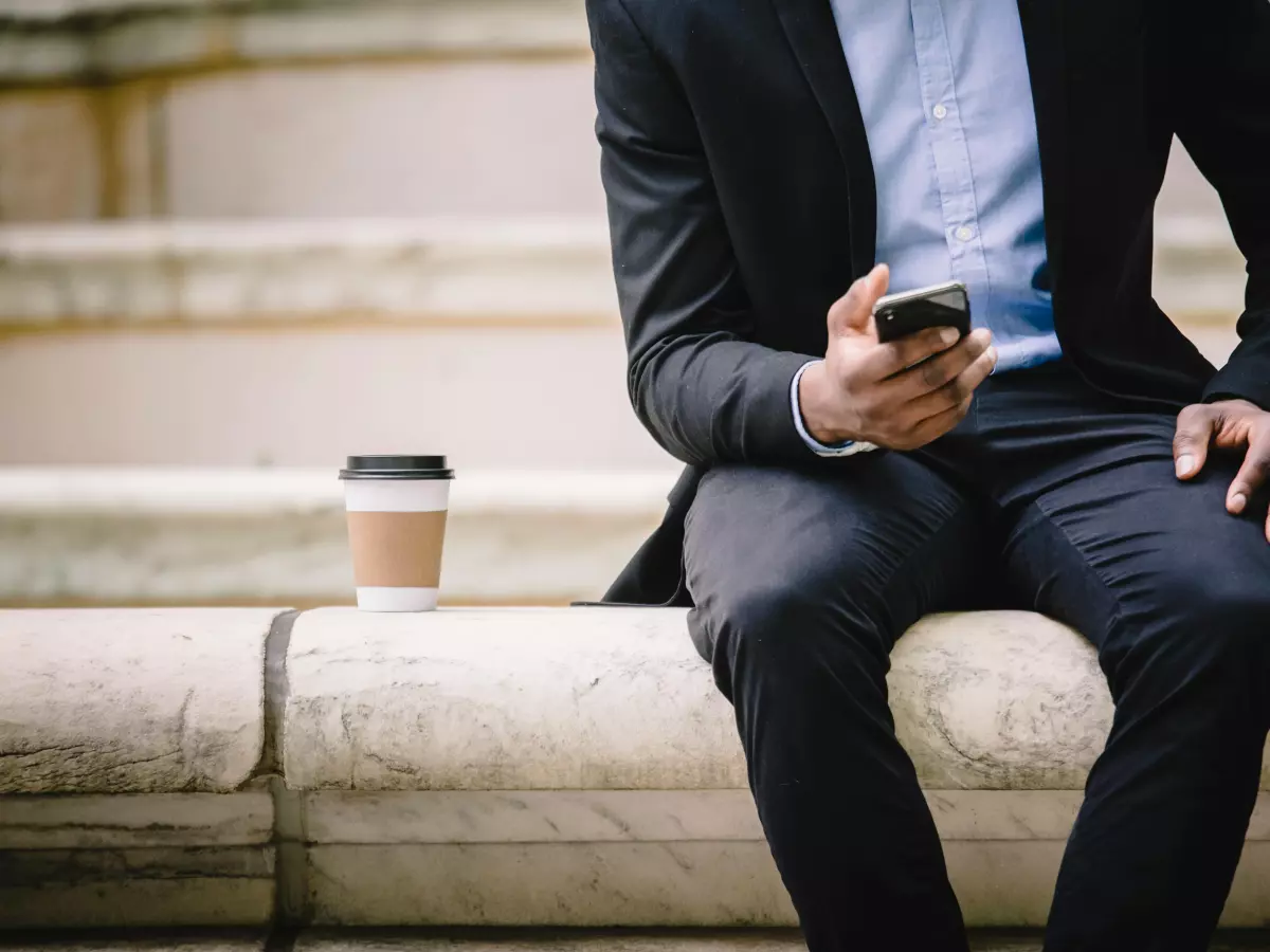 A person in a business suit is sitting on a stone wall and using a smartphone.