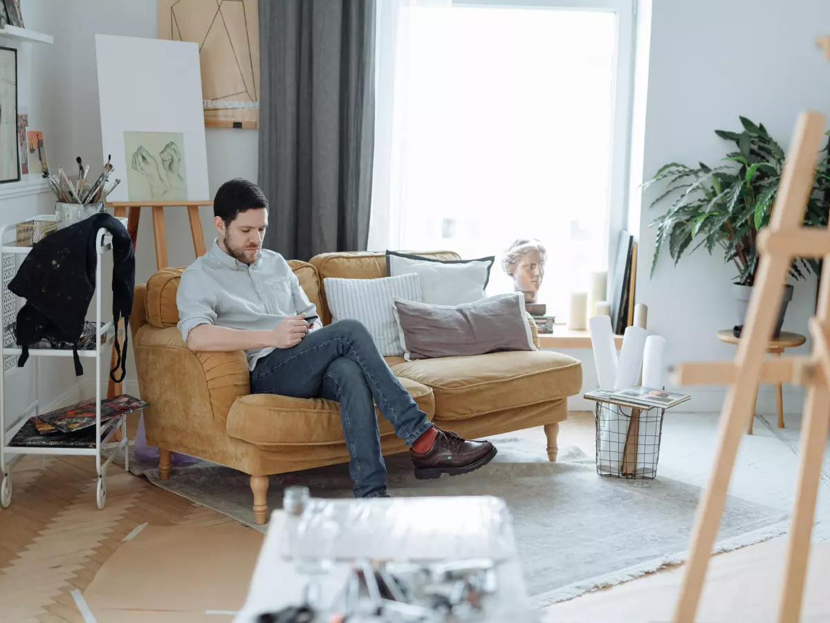 A young man is sitting on a sofa, using his phone,  the image is well lit,  with warm colors and soft focus,  adding to the feel.