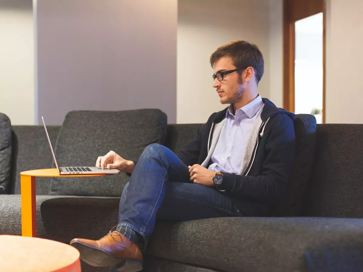 A man in glasses sitting on a sofa using a laptop