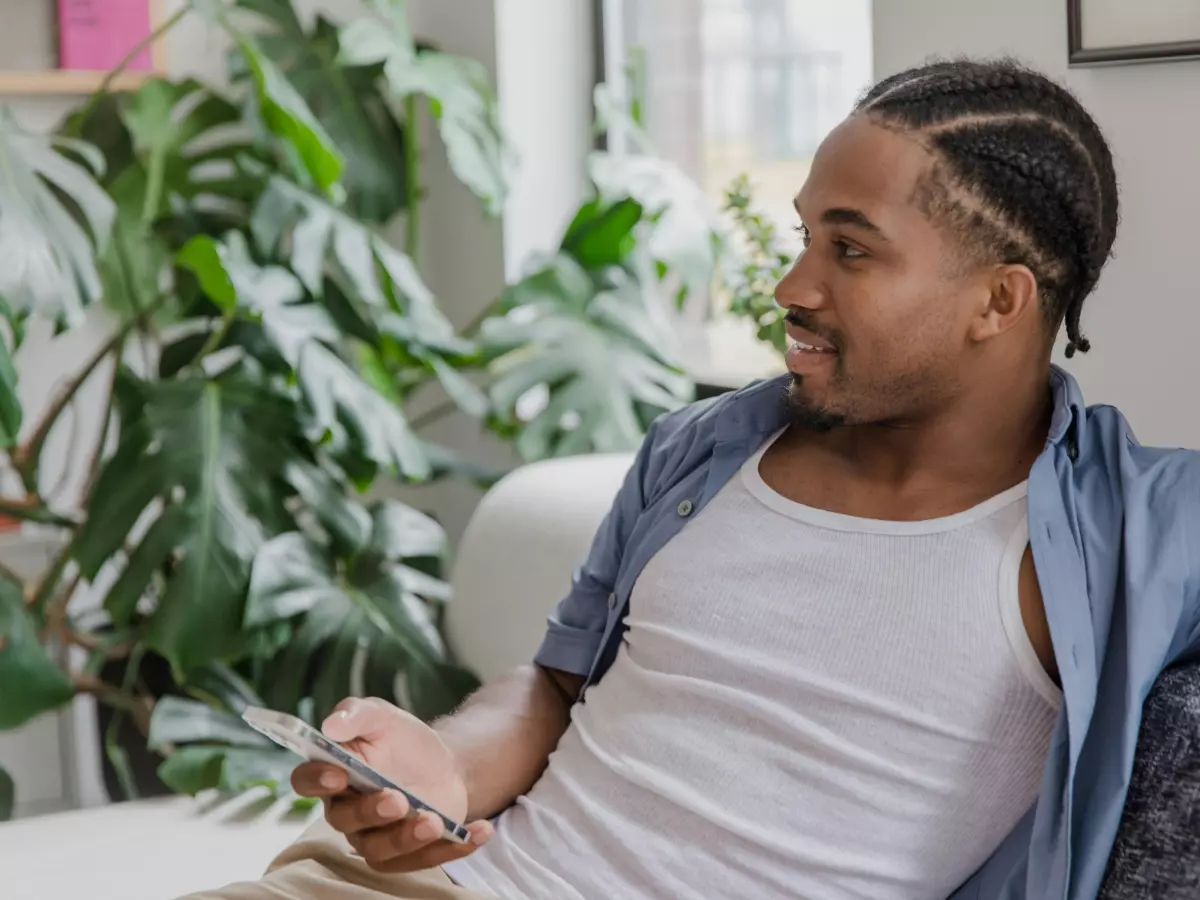 A person is sitting on a sofa and holding a smartphone. The person is looking at the phone and smiling.