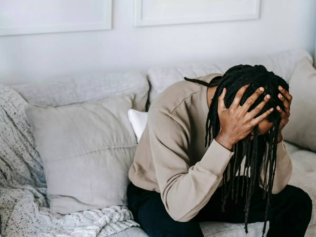 A person with their head in their hands, sitting on a couch, looking distressed.