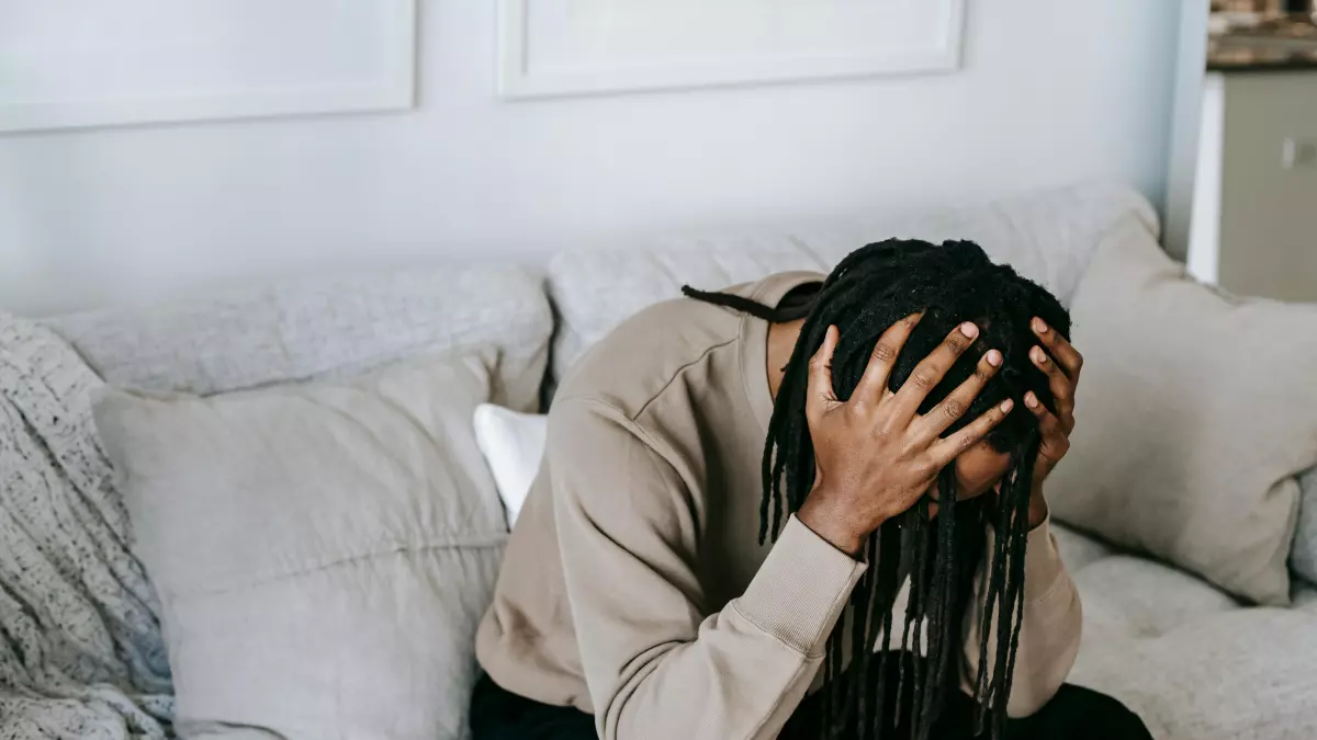 A person with their head in their hands, sitting on a couch, looking distressed.