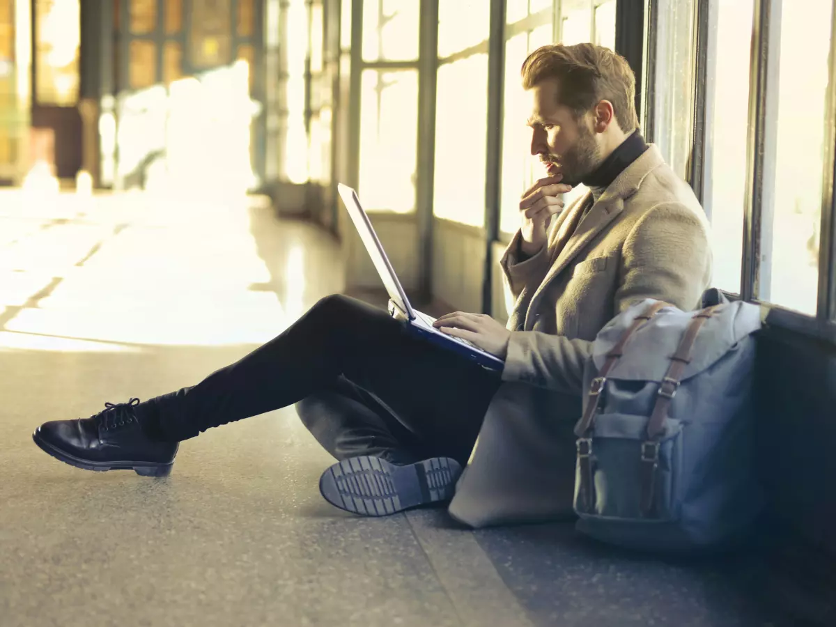 A man sits on the floor in a building, working on his laptop.