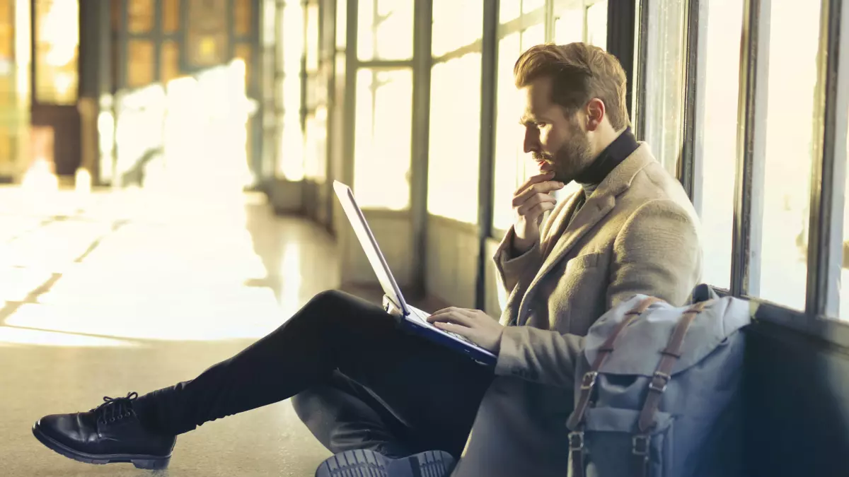 A man sits on the floor in a building, working on his laptop.