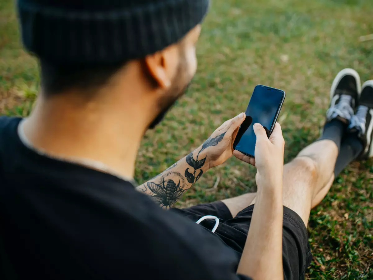 A person is using their smartphone while sitting on the grass. The image is taken from behind the person, and their face is not visible.