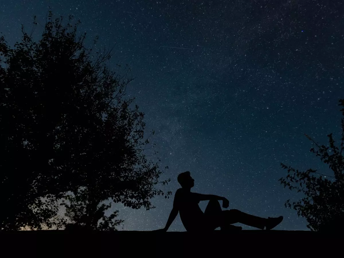 A silhouette of a person sitting under a starry night sky.