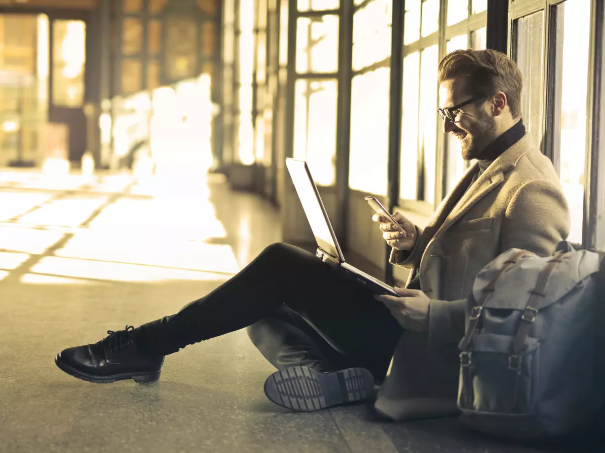 A man sitting on the floor, using a laptop and a smartphone.