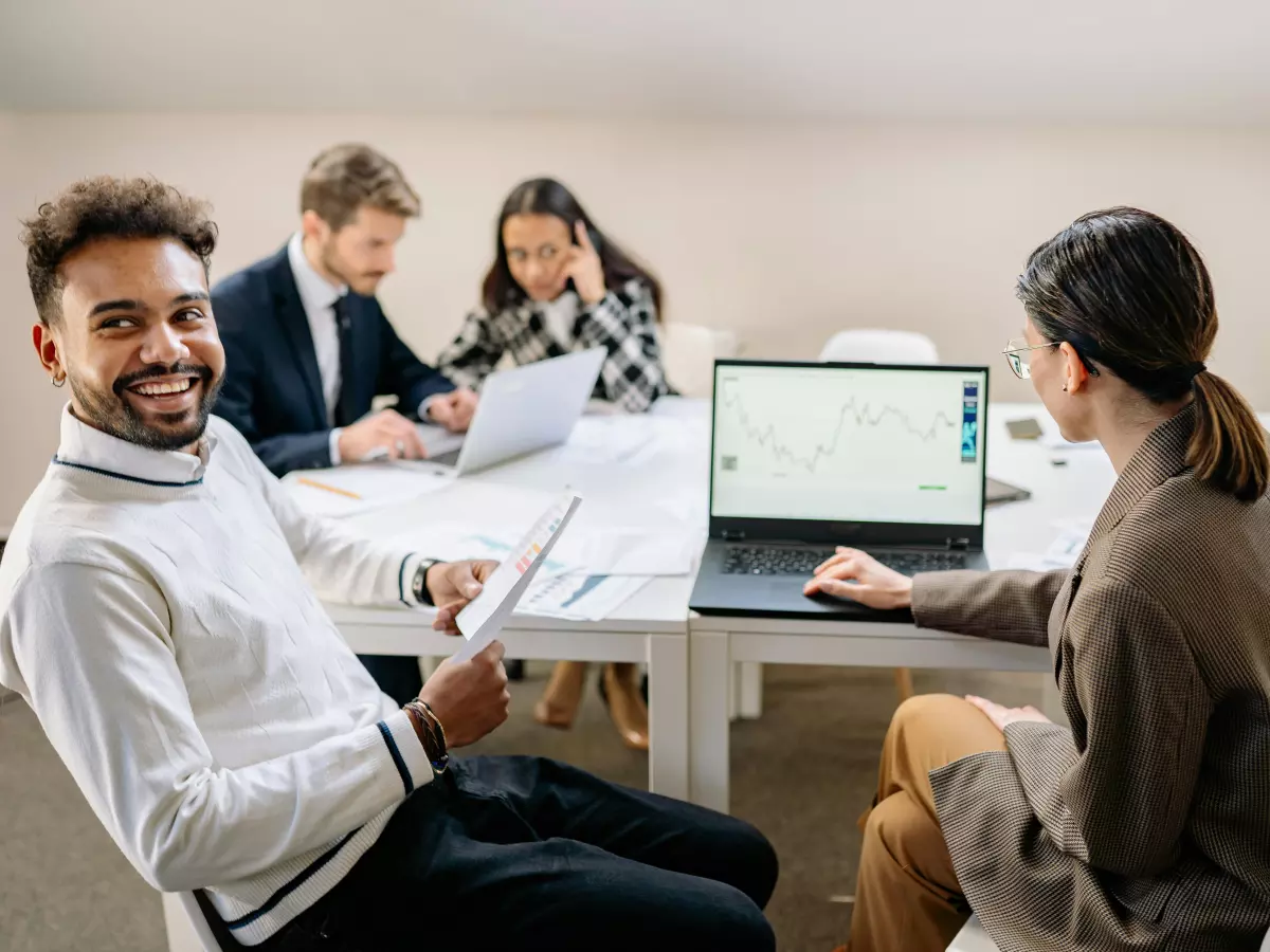 Four people sitting around a table, working on laptops. One person is smiling at the camera.